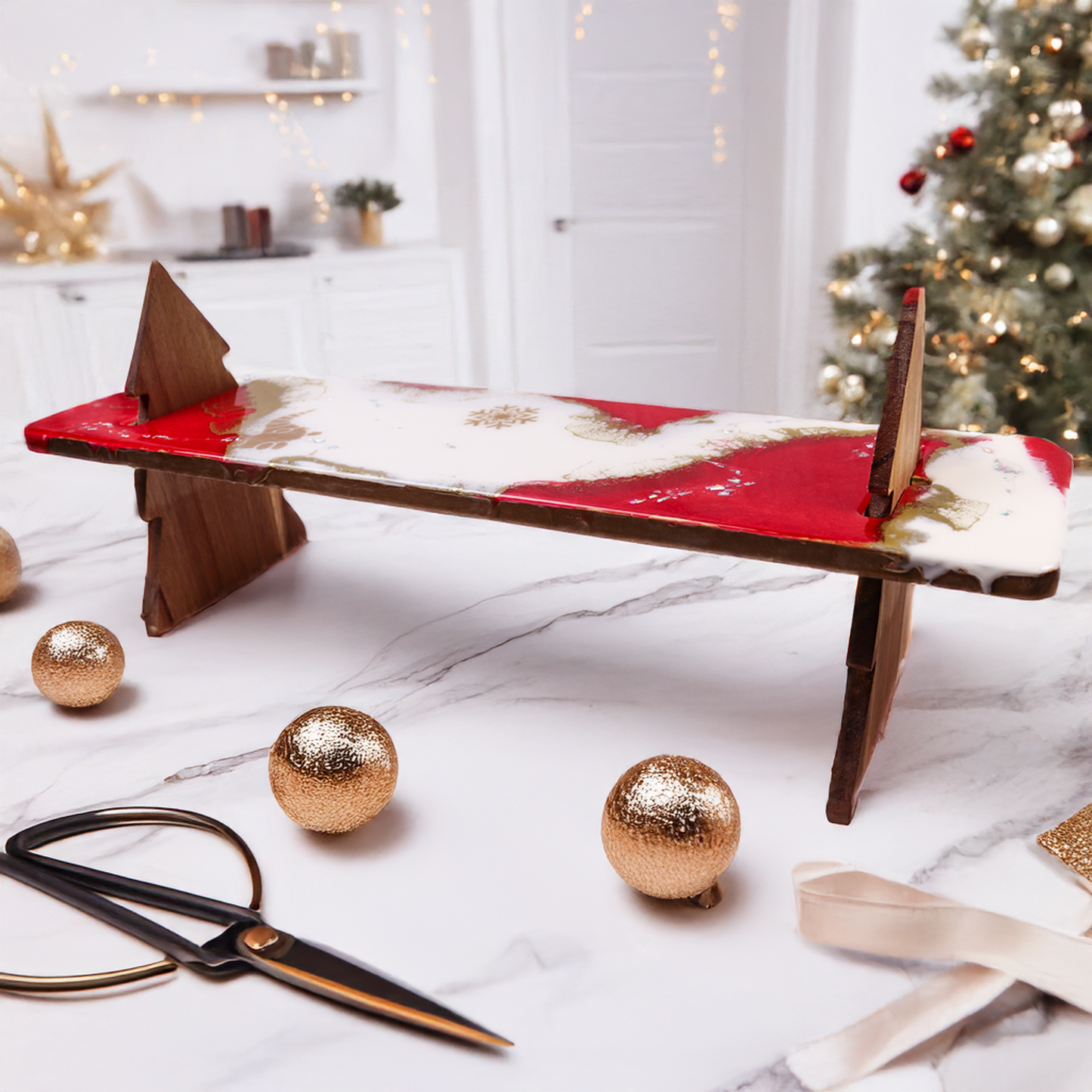 Festive WildArt Christmas lap serving tray made from Acacia wood with resin coating, featuring a red, white, and gold holiday design. The tray is supported by Acacia wood legs shaped like Christmas trees, perfect for serving cheese and holiday treats. Set against a cosy, holiday-themed background with decorative gold ornaments and ribbon, capturing the warmth of the season.